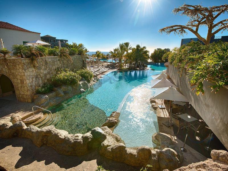 Piscina de lujo con elementos de piedra natural y sombrillas en un lugar soleado de vacaciones.