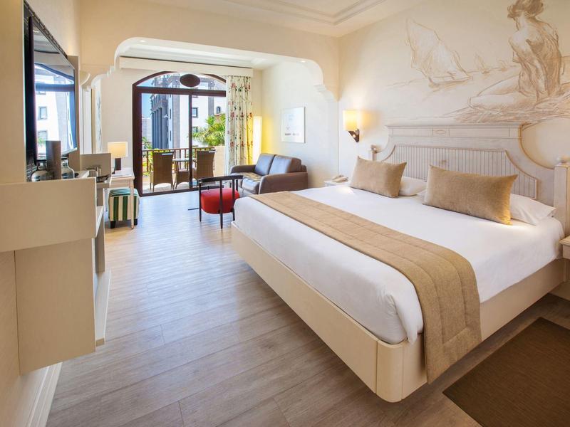 Habitación de hotel luminosa con cama grande, ventana a la terraza e interior moderno.