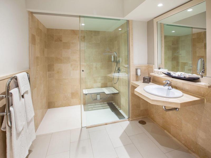 Baño moderno con ducha a ras de suelo, gran espejo y lavabo en tonos beige y blanco.