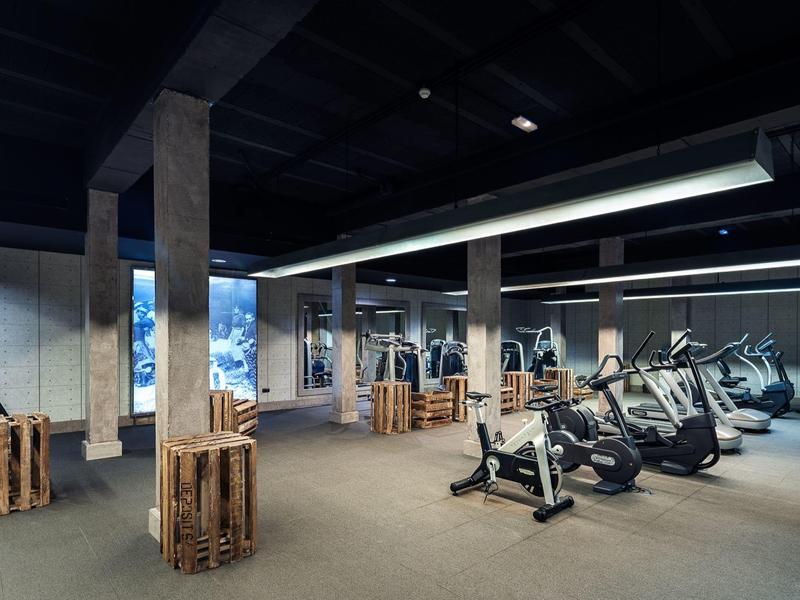 Gimnasio moderno con máquinas de cardio, moqueta gris y paredes de espejos en un hotel.