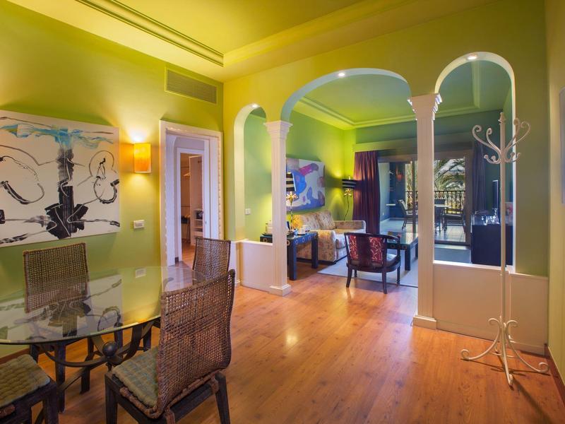 Interior de habitación de hotel luminosa con paredes verdes, suelo de madera y mobiliario moderno.