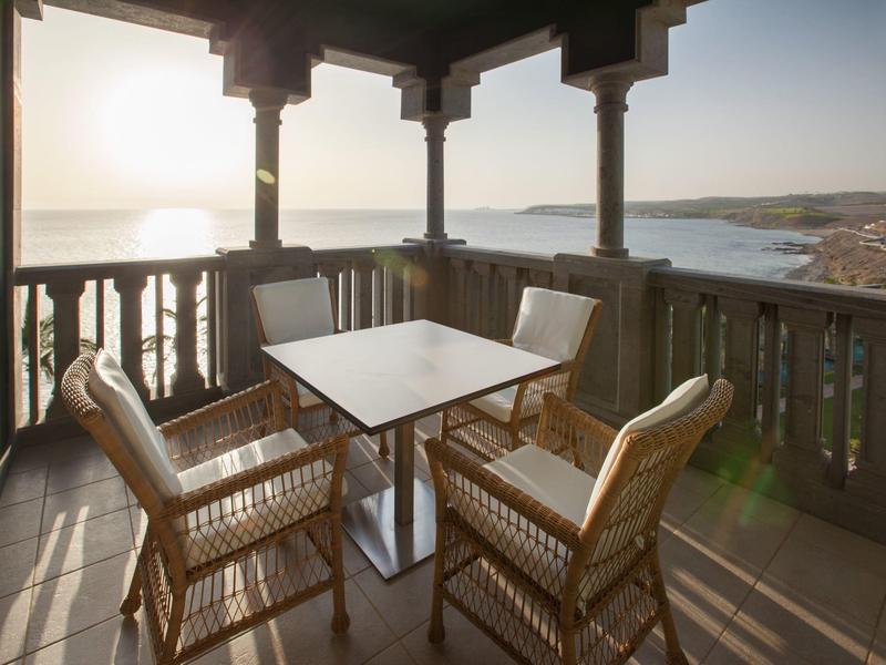 Balcón con muebles de madera y vista al mar al atardecer en un hotel.