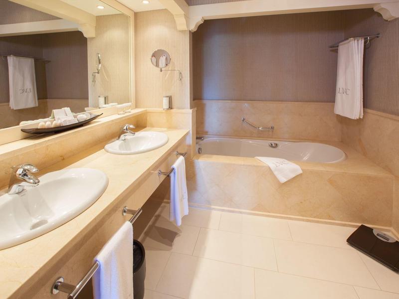 Baño luminoso con lavabo doble, bañera y espejos grandes en tonos cálidos.