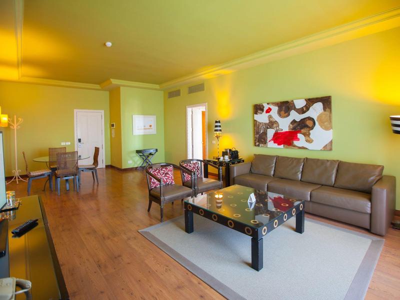 Sala luminosa con sofá de cuero marrón, mesa de vidrio y arte colorido en la pared de una habitación de hotel.