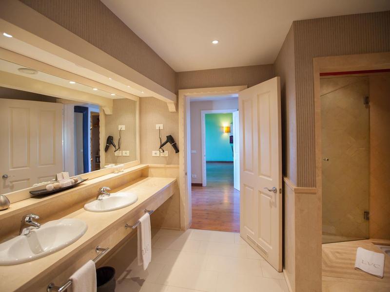 Baño moderno con doble lavabo, espejo grande y ducha junto a la puerta abierta.