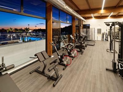 Gimnasio con equipo cardiovascular y vista a la piscina al anochecer