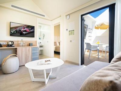 Modern eingerichtetes Wohnzimmer mit hellen Möbeln, TV, rundem Tisch und Zugang zur Terrasse.