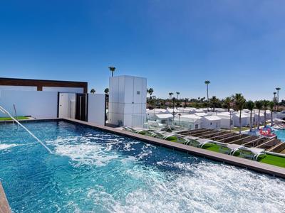 Hotel moderno con piscina y jacuzzi bajo un cielo azul despejado