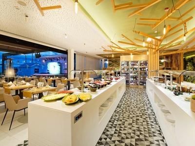 Moderner Speisesaal mit Buffet, Holzdecke, großen Fenstern und hellen Tischen.