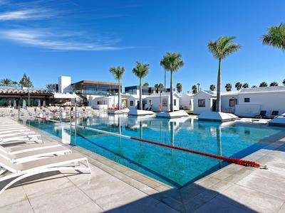 Moderner Poolbereich mit weißen Liegestühlen, Palmen und klarem blauem Himmel bei Sonnenschein.