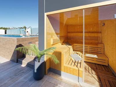 Sauna mit Glasfront auf heller Holzterrasse, moderner Stil, Pflanzen neben dem Eingang.