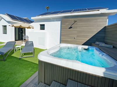 Moderner Garten mit Whirlpool, zwei Liegestühlen und Solarpaneelen auf dem Hausdach.