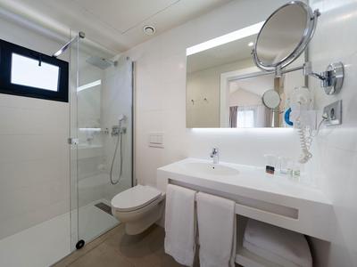 Modernes Badezimmer mit Glasdusche, weißem Waschtisch, Wandspiegel und hängendem Kosmetikspiegel.