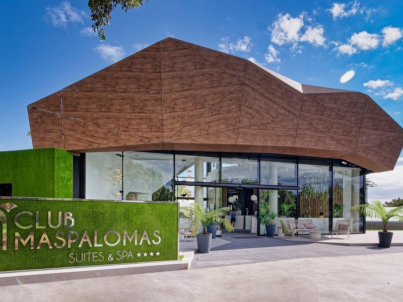 Modernes Clubhaus mit markanter brauner Fassade, großen Glasfronten und grünem Eingangsschild.