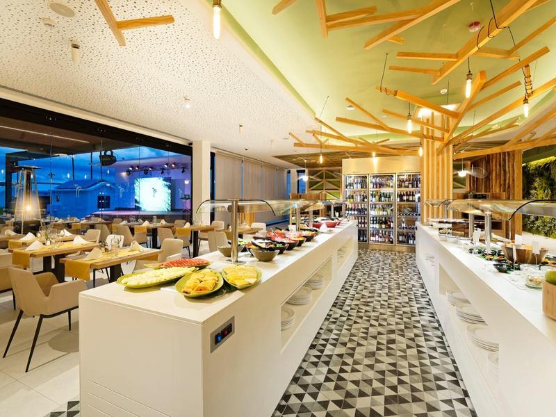 Moderner Speisesaal mit Buffet, Holzdecke, großen Fenstern und hellen Tischen.