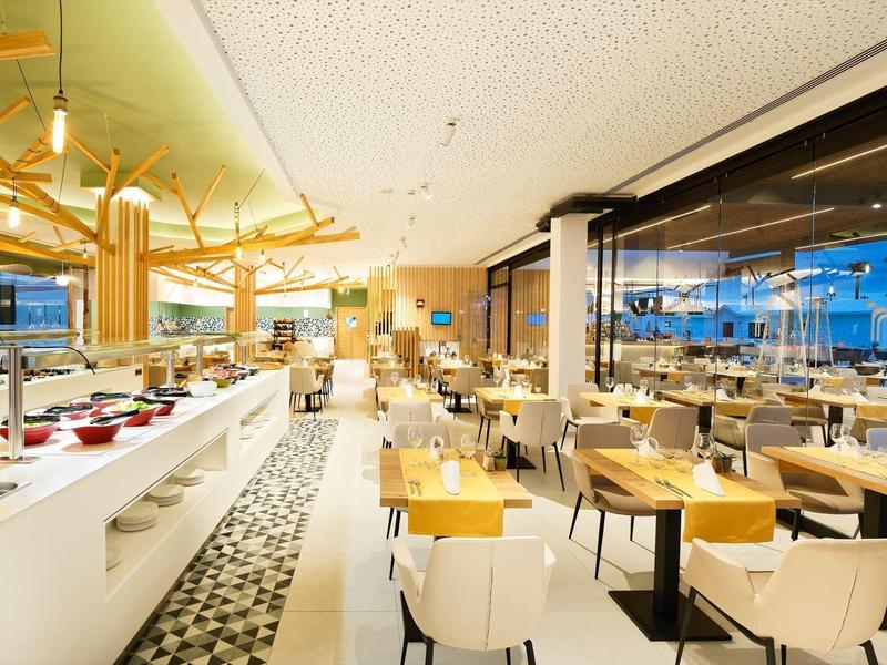 Modernes Restaurant mit hellem Ambiente, Tischen, Stühlen und Buffetbereich am Fenster.