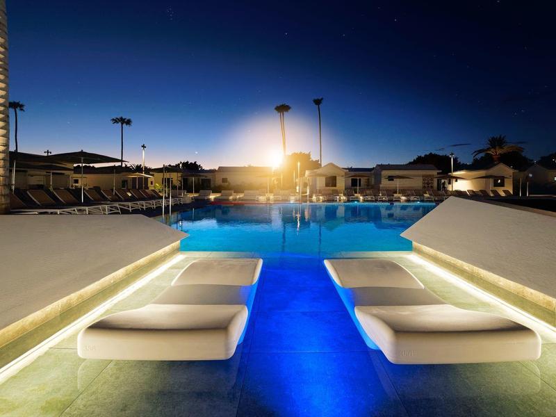 Moderner Pool mit beleuchteten Liegen, blauem Wasser und warmem Licht bei Nacht.