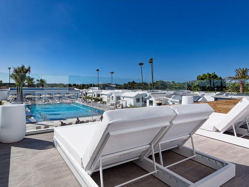 Moderne Dachterrasse mit weißem Lounge-Möbel, Pool und klarem blauem Himmel im Hintergrund.