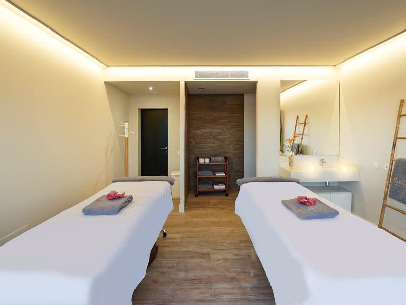 Moderner Behandlungsraum mit zwei weißen Liegen, Holzfußboden und warmem LED-Licht.