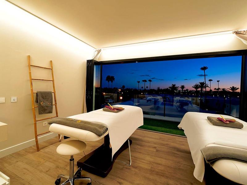 Modernes Behandlungszimmer mit zwei Liegen, Holzboden und großer Fensterfront mit Abendblick.