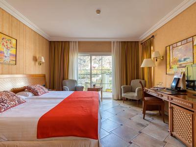 Hell eingerichtetes Hotelzimmer mit zwei Betten, oranger Bettdecke und Zugang zum Balkon.