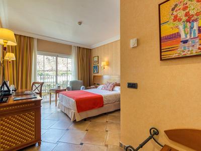 Helles Hotelzimmer mit Doppelbett, roten Akzenten, Schreibtisch, Balkon und gemaltem Wandbild.