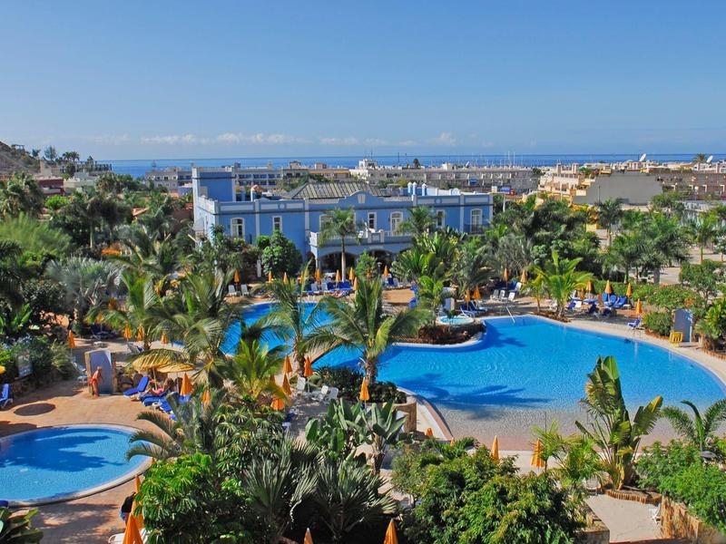 Outdoor resort pool area surrounded by palm trees with sea and city view.