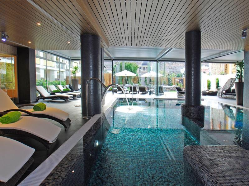 Indoor pool area with lounge chairs and large windows letting in natural light.