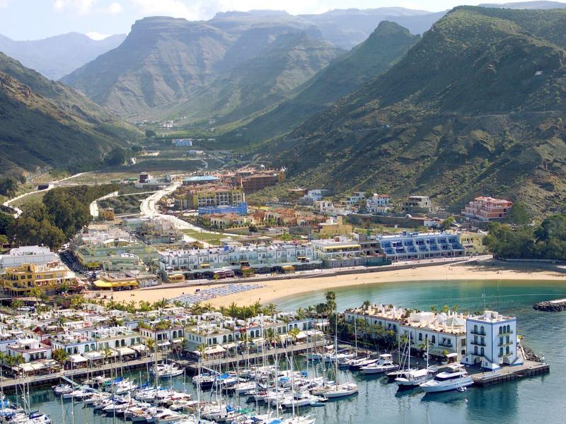 Marina with boats, hotels, and mountains in the background under a clear sky.