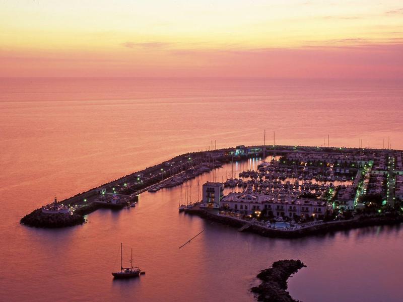 A harbor with boats at sunset, vibrant orange and pink sky over calm sea.