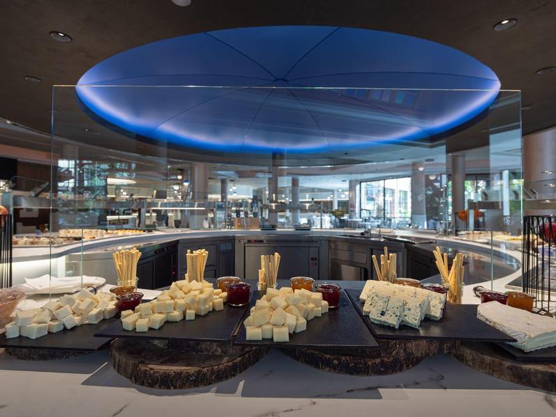 Modern buffet setup with cheeses, breads, and a glowing blue circular ceiling light in an elegant dining area.