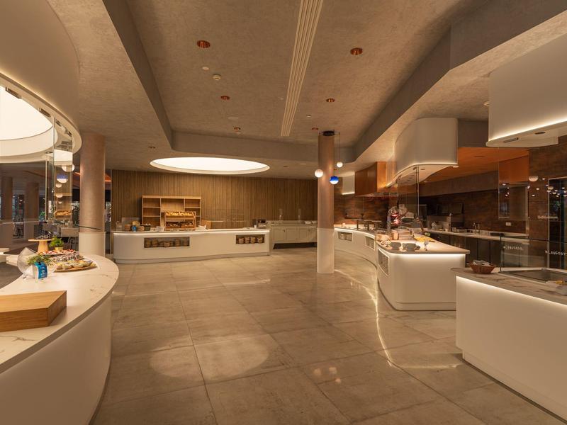 Spacious, modern kitchen area with beige tiles, white countertops, and warm lighting.
