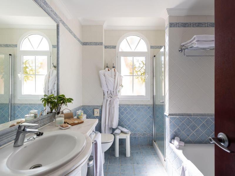 Bright bathroom with large window, white sink, bathtub, and blue tile accents.