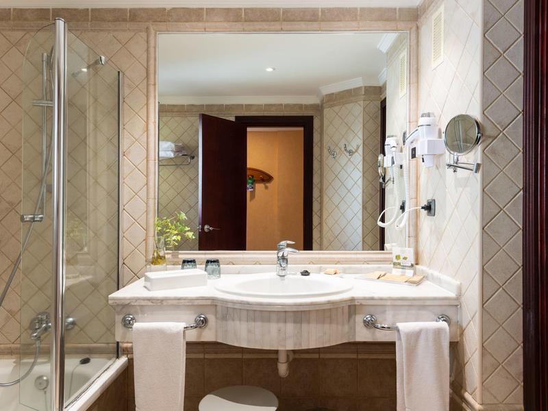 Hotel bathroom with large mirror, sink, towels, and glass shower enclosure.
