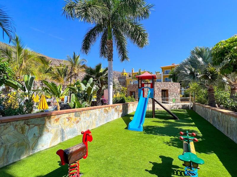 Outdoor playground with slides and palm trees under a clear blue sky