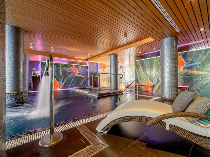 Modern indoor pool area with loungers, colorful wall art, and ambient lighting.
