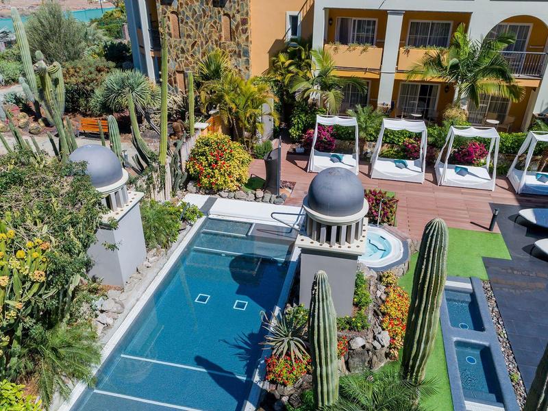 Outdoor pool area with lush greenery and sun loungers at a hotel courtyard.