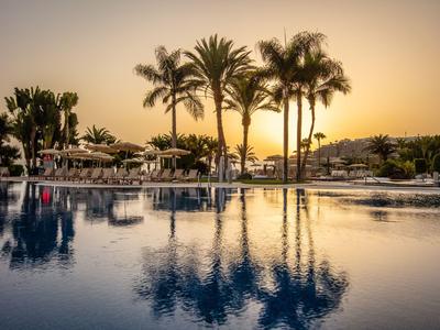 Ein ruhiger Pool mit Palmen und Sonnenschirmen bei Sonnenuntergang.