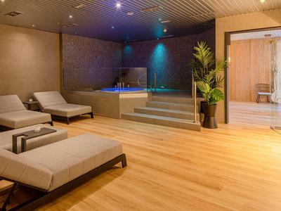 Moderní wellness s dřevěnou podlahou, lehátky a osvětlenou vířivkou.