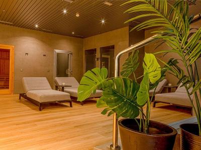 Klidná wellness zóna s lehátky a rostlinami na světlé dřevěné podlaze.