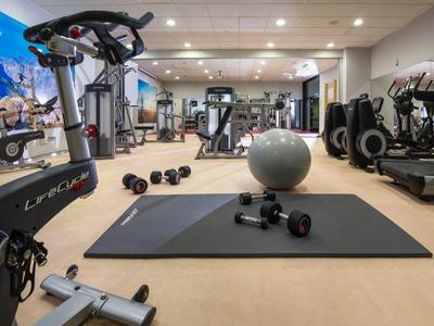 Moderner Fitnessraum mit Trainingsmatte, Hanteln, Laufbändern und Gymnastikball.