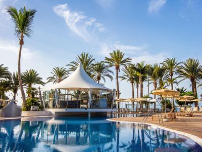 Luxusní bazénová zóna s bílými stany, palmami a modrou oblohou v rezortu.