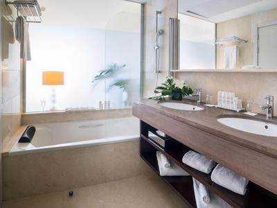 Moderní koupelna s vanou, umyvadlem, velkým zrcadlem a měkkými ručníky.