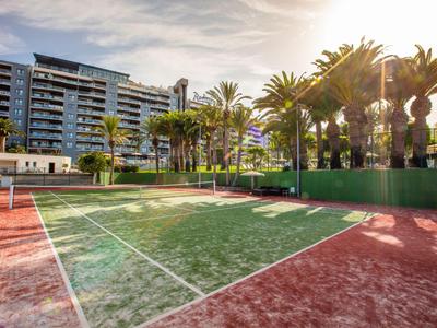 Tennisplatz vor einem modernen Hotel mit Palmen und Sonnenuntergang im Hintergrund