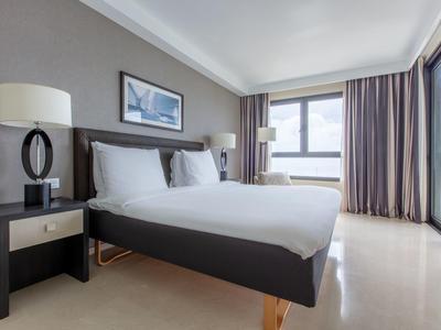 Světle zařízený hotelový pokoj s velkou postelí a oknem se závěsy.