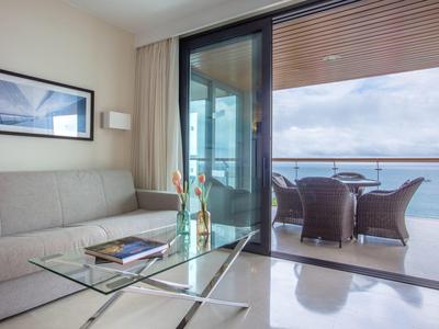 Moderní obývací prostor se skleněným konferenčním stolkem, pohovkou a balkonem s výhledem na moře.