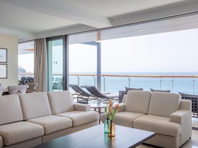 Světlý salón s béžovými pohovkami a výhledem na balkon s lehátky a mořem.