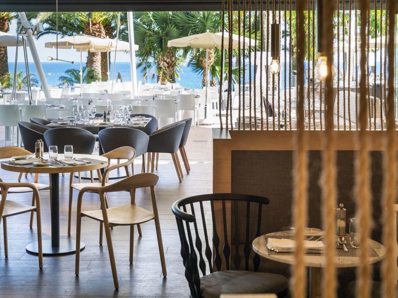 Příjemná hotelová část s stoly, židlemi a výhledem na bazén a slunečníky.