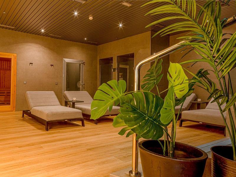 Klidná wellness zóna s lehátky a rostlinami na světlé dřevěné podlaze.