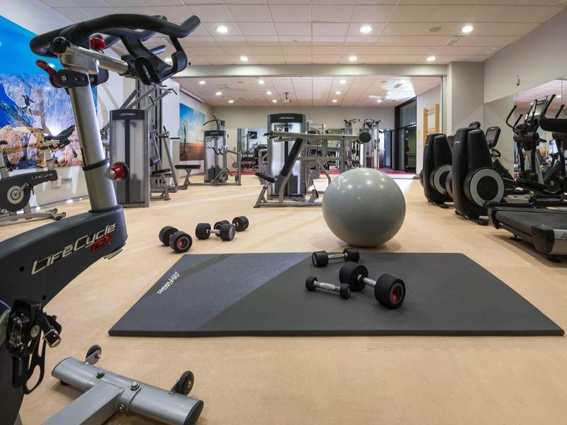 Moderní posilovna s cvičební podložkou, činkami, kardio stroji a zrcadlovou stěnou.